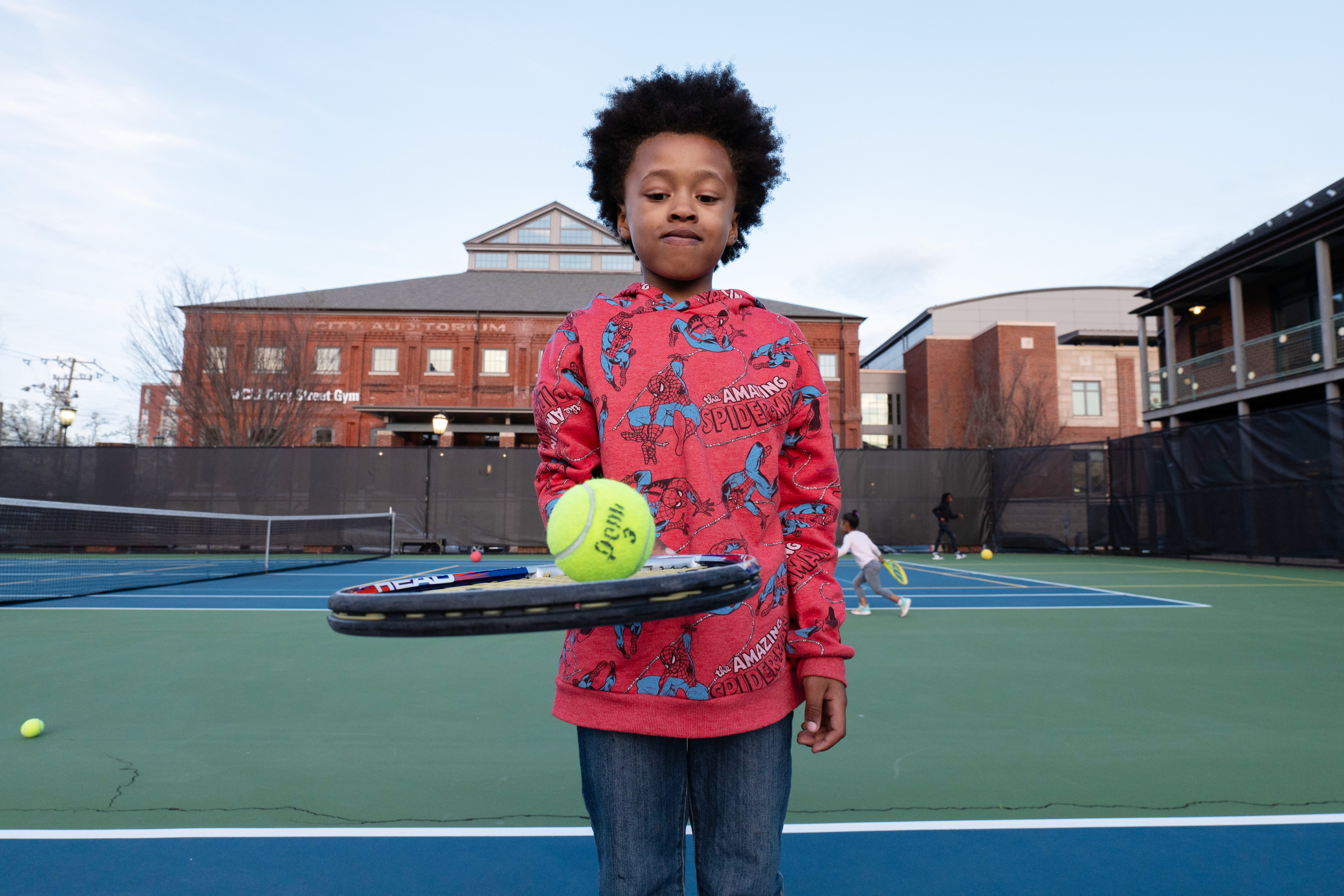 A young boy on the tennis court with a tennis bat and ball